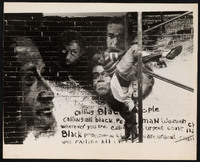  Black and white photo of 2 boys playing on scaffolding in front of a mural painted on a brick wall.