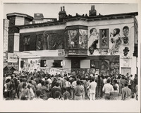 Black and white photo of a large crowd looking at a building covered in murals.