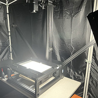 The copy stand with the transparency top installed. One light has been removed from its stand and is underneath the top. The other remains in position. Both are lit.
